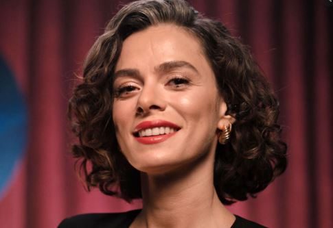 Özge Özpirinçci Betimleyen: Cem OCAKLAR (Çukurova Üniversitesi öğrencisi) Yatay dikdörtgen, renkli, yakın çekim portre fotoğrafta Özge Özpirinçci, kafasını hafif sağına çevirerek doğrudan objektife bakarak gülümsüyor. Fonda kırmızı bir perdenin olduğu fotoğrafta Özpirinçci’nin çok az kadraja giren omuzlarından siyah bir kıyafet giydiği anlaşılıyor. Fotoğrafta 30’lu yaşların ortasında görünen Özge Özpirinçi, boynunun orta kısmını geçen ve omuzlara yaklaşan, üstü dalgalı alt kısımları kıvırcık saçlara sahip. Saçları, sağ kulağının tamamını sol kulağının yarısını kapatıyor. Sol kulağında küpe gözüküyor. Altın renkli küpesi, kulak memesi büyüklüğünde yukarıdan aşağı doğru birbirine yakın genişleyerek artan daireler şeklinde. Kahverengi saçları, alnının sol kısmını çok az kapatıyor. Alnının geri kalanı tamamen görünüyor. Sağ kaşına saçı değiyor. Yüz hatları oval ve kulak hizasından çeneye doğru daralma mevcut. Kırmızı rujlu dudağıyla gülümserken beyaz, düzgün üst dişleri gözüküyor. Dişleri ile alt dudakları arasında hafif boşluk var. Burnu düz, burun tabanı genişçe. Badem şeklindeki gözleri siyah. Sol gözü daha kısık. Uzun bir boynu var. Çenesi, sağ yanağı ve alnının ortası ışıktan dolayı parlıyor. Çenesinin gölgesi boynunun üst bölümünün az bir kısmını kaplıyor.  Burun delikleri net olarak gözüküyor.