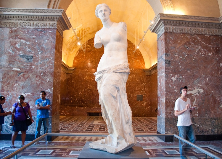 Venus De Milo Venus De Milo heykeli bir buçuk insan boyu yükekliğinde, beyaz mermerden yapılmış, çıplak kadın figürü. Kare bir bloğun üzerinde ayakta duran kadının vücudu hafif sağa kıvrılmış. Belki 20’lerinde kadının dik ve iri sayılmayan memeleri var. Meme uçları belirgin. Karnı gergin ve karın kasları hafif belli oluyor. İrice ve yuvarlak bir göbek deliği var. Belinin altından, tam cinsel organının üzerinden ayaklarına kadar alelade örtülmüş gibi duran bir örtü ile kaplı. Örtünün altından sadece sağ ayağının baş ve ikinci parmağı görünüyor. Sol bacağı biraz daha önde duran kadının dizi kendine doğru hafif kırılmış. Dolayısıyla sol kasığı daha derin belli oluyor. Heykelin sol kolu tam omuzdan, sağ kolu ise meme hizasından kopmuş.  Hafif sağa eğik başında kıvırcık, ortadan ayrılmış, kısa saçları var. Gözleri açık ve dudakları kapalı. Yüzüne göre büyük olmayan bir burnu ve belirgin bir çenesi var. Vücuduna oranla küçük yüzlü olan heykelin yüz ifadesi donuk.