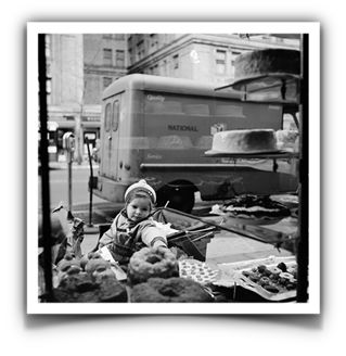 Fotoğrafın Adı Bilinmiyor Fotoğrafçı: Vivian Maier  Betimleyen: Serra ULUSOY  (Boğaziçi Üniversitesi, ED200 dersi öğrencisi)  Siyah beyaz dikey dikdörtgen fotoğrafta bebek arabasından sokaktaki kurabiye tezgahına uzanan bir çocuk yer alıyor. Fotoğrafın  sağında ve solunda boydan boya beyaz çerçevesi var.  Fotoğrafın en altında, en yakındaki tezgahta kekler, pastalar ve çörekler duruyor. Fotoğrafın tam ortasından bir-iki santim solda kalan bir bebek, eski tarz bebek arabasında pastalara bakıyor ve oturuyor . Çocuğun yüzü bize dönük ve çocuğun durduğu kaldırımın arkasındaki yoldan bir kamyon geçiyor.  Çocuk yuvarlak bir bere takmış ve mont giymiş bebek arabasında oturmakta. Saçları şapkasından bir santim çıkmış görülüyor. Yüzü yuvarlak ve alnı geniş.  Fotoğrafın sağ tarafı boydan boya raflarla dolu ve pastalar görülüyor. Dört tane rafta pastalar dairesel şekilde. En alttaki rafta minik çörekler var. İkinci rafta siyah ve beyazlı tatlı görülmekte. Üçüncü ve dördüncü raflarda dairesi pasta var.  Çocuğun arkasındaki yoldan kamyon geçmekte. Karşı kaldırımda iki binanın da yarısı görülüyor. Binaların camları boyuna dikdörtgen şeklinde.