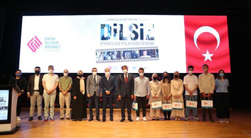 Bir tiyatro sahnesinde çekilen fotoğrafta, barkovizyona yansıtılan görselde Dilsiz filmi  Engelsiz Film Gösterimi yazıyor. Sahnedeki kadınlar ve erkekler yan yana durmuş, objektife bakıyor.