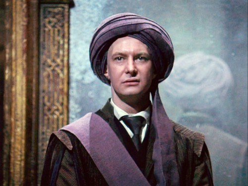Harry Potter And The Philosopher`s Stone / Harry Potter Felsefe Taşı Filmi - Quirinus Quirrell  Filmden bir kare olduğu anlaşılan yatay dikdörtgen şeklindeki fotoğrafın ortasında Quirinus Quirrell (Ian Hart) yüzünde tiksinmiş bir ifadeyle yukarı doğru bakıyor.  Quirrell, otuzlu yaşlarının ortalarında gözüken bir erkek. Beyaz bir ten rengine sahip. Kafasında defalarca sarılmış mor renkli bir eşarp var. Kulaklarının yarısı bu sarığın arkasında kalmış. Eşarbın ucu önünden aşağı doğru sarkıyor. Sarkan uç sonrasında sağ omuzun üzerine düz bir biçimde atılmış.  Oval bir yüzü ve seyrek kaşları var.  Küçük gözleri yukarı doğru bakıyor. İnce burnunun kenarlarından dudak çevresine doğru çizgiler belirmiş. Soluk renkte dudakları hafif aralanmış ve sola doğru yukarı kalkmış, bu hareketi yüzüne tiksinmiş bir ifade vermiş.  Düz bir çenesi var.  Beyaz renkte gömleğinin üzerine siyah bir kravat takmış. Üzerine kahverengi bir pardösü giymiş. Arka planda kenarlarında altın rengi işlemeler bulunan puslu bir ayna var. Aynada Quirrell’in arkasının yansıması gözüküyor.